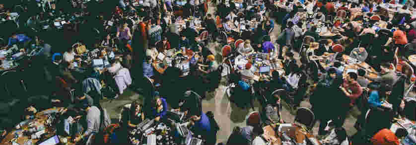 Large room of students at tables participating in a hackathon